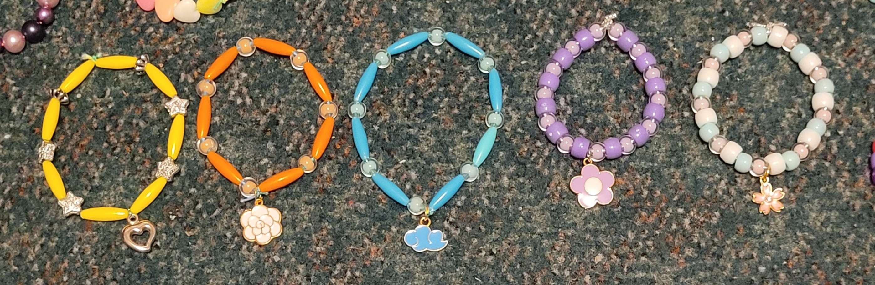 Five beaded single bracelets, each with a charm in the middle.