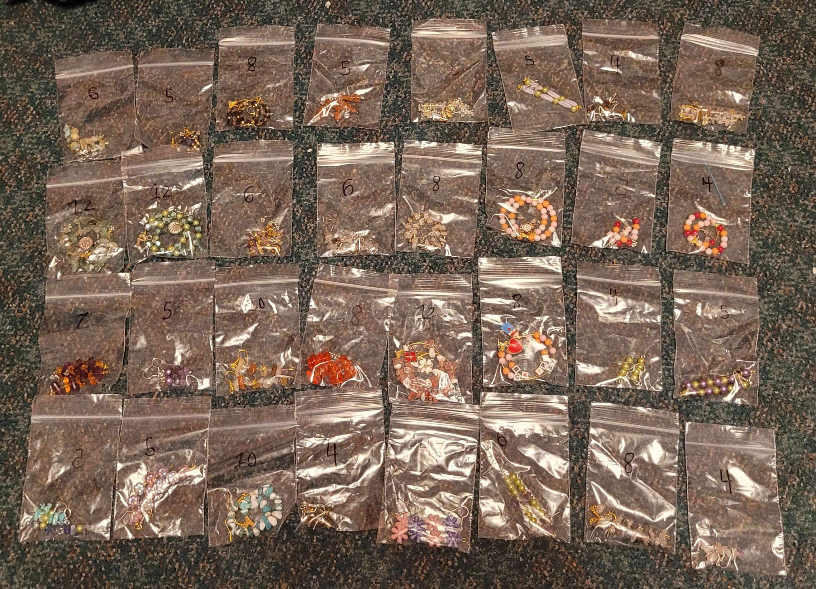 An organized pile of various earrings, each in small clear bags.