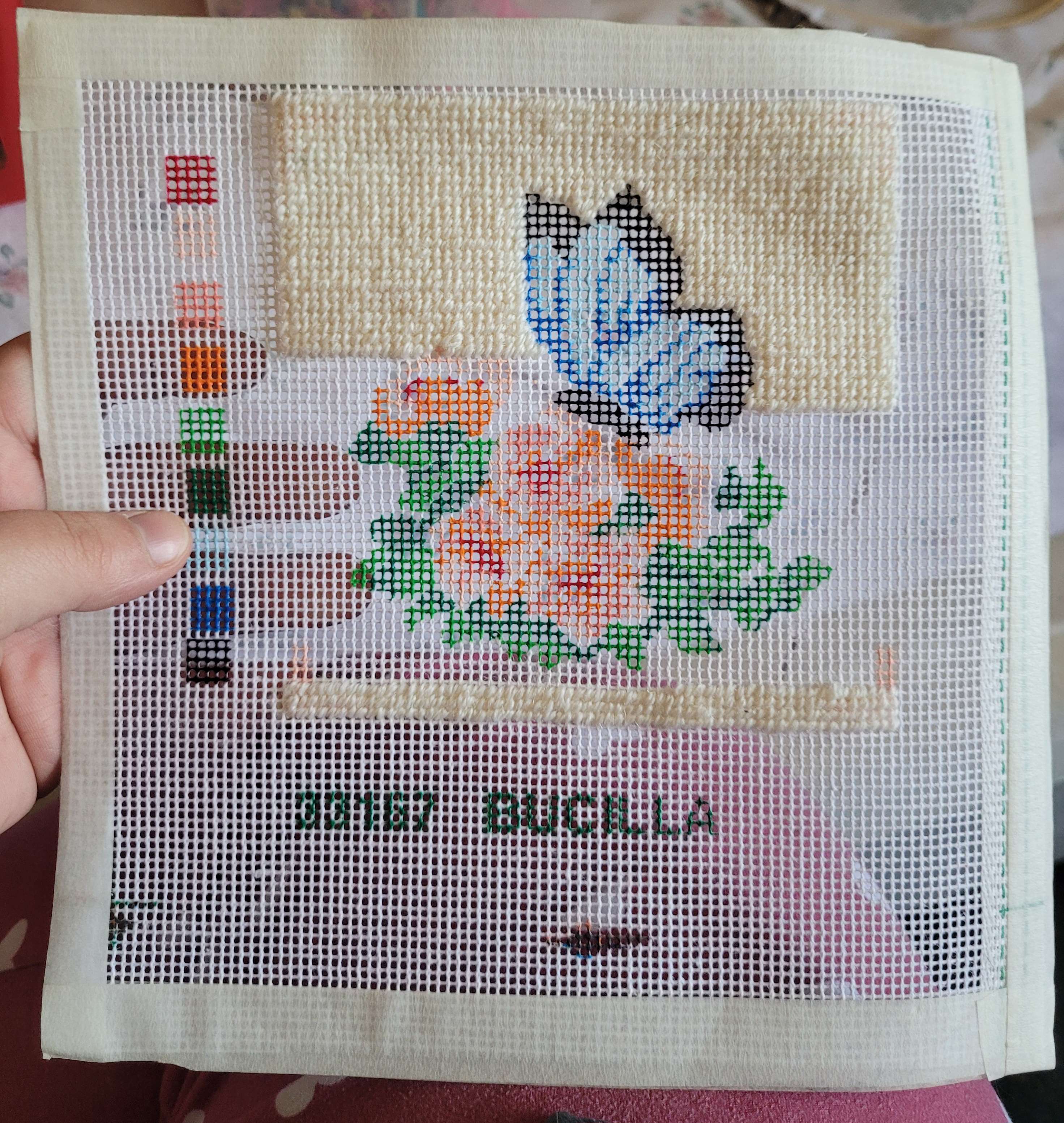 A partially completed needlepoint of a white butterfly.